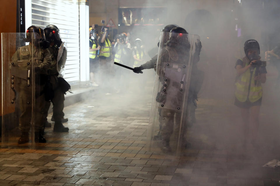 Riot police form up as journalists work nearby amongst tear gas in Hong Kong on Saturday, Aug. 3, 2019. Hong Kong protesters removed a Chinese national flag from its pole and flung it into the city's iconic Victoria Harbour on Saturday, and police later fired tear gas at demonstrators after some of them vandalized a police station. (AP Photo/Vincent Thian)