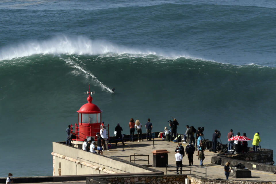 People on the top of the lighthouse watch a surfer ride a wave during a tow surfing session at Praia do Norte or North Beach in Nazare, Portugal, Thursday, Oct. 29, 2020. A big swell generated earlier in the week by Hurricane Epsilon in the North Atlantic, reached the Portuguese west coast drawing big wave surfers to Nazare. (AP Photo/Pedro Rocha)