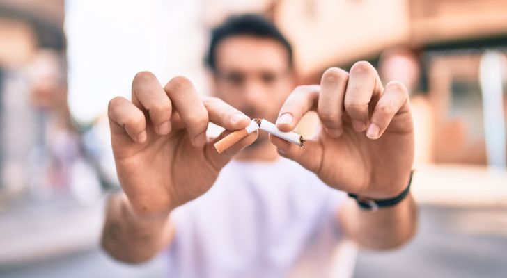 young man breaks a cigarette while walking on the city streets. Promotes quitting smoking.