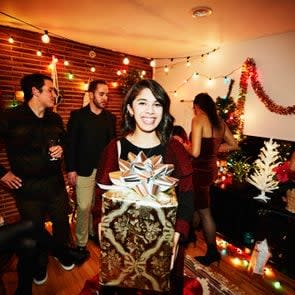 Smiling woman holding present during holiday party with friends in home