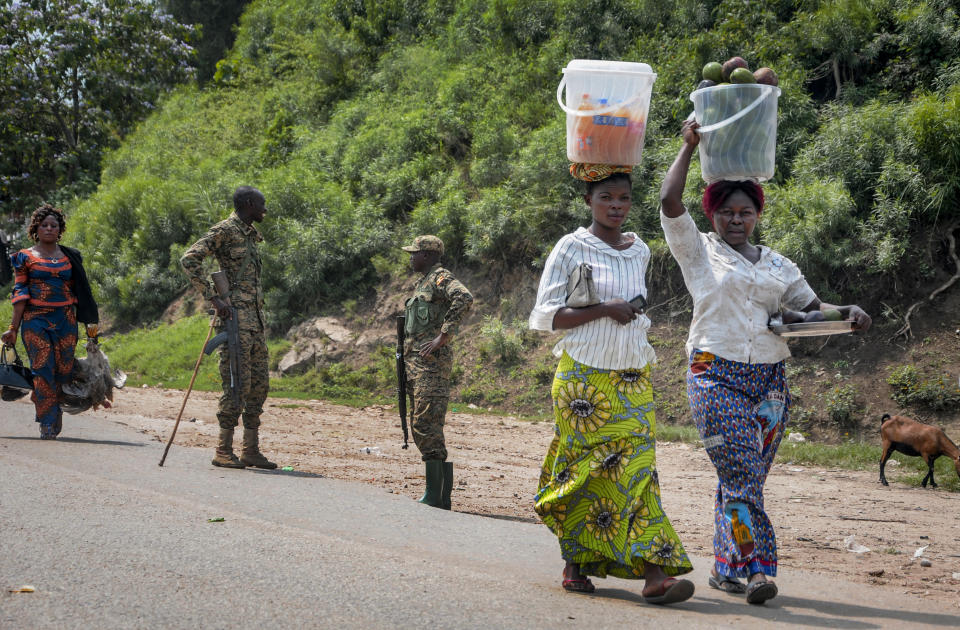 Two women heading towards Congo carry food on their heads as they walk past Ugandan army soldiers ensuring those crossing the border do not do so without being screened for symptoms of Ebola, at the Mpondwe border crossing to Congo, in western Uganda Friday, June 14, 2019. In Uganda, health workers had long prepared in case the Ebola virus got past the screening conducted at border posts with Congo and earlier this week it did, when a family exposed to Ebola while visiting Congo returned home on an unguarded footpath. (AP Photo/Ronald Kabuubi)