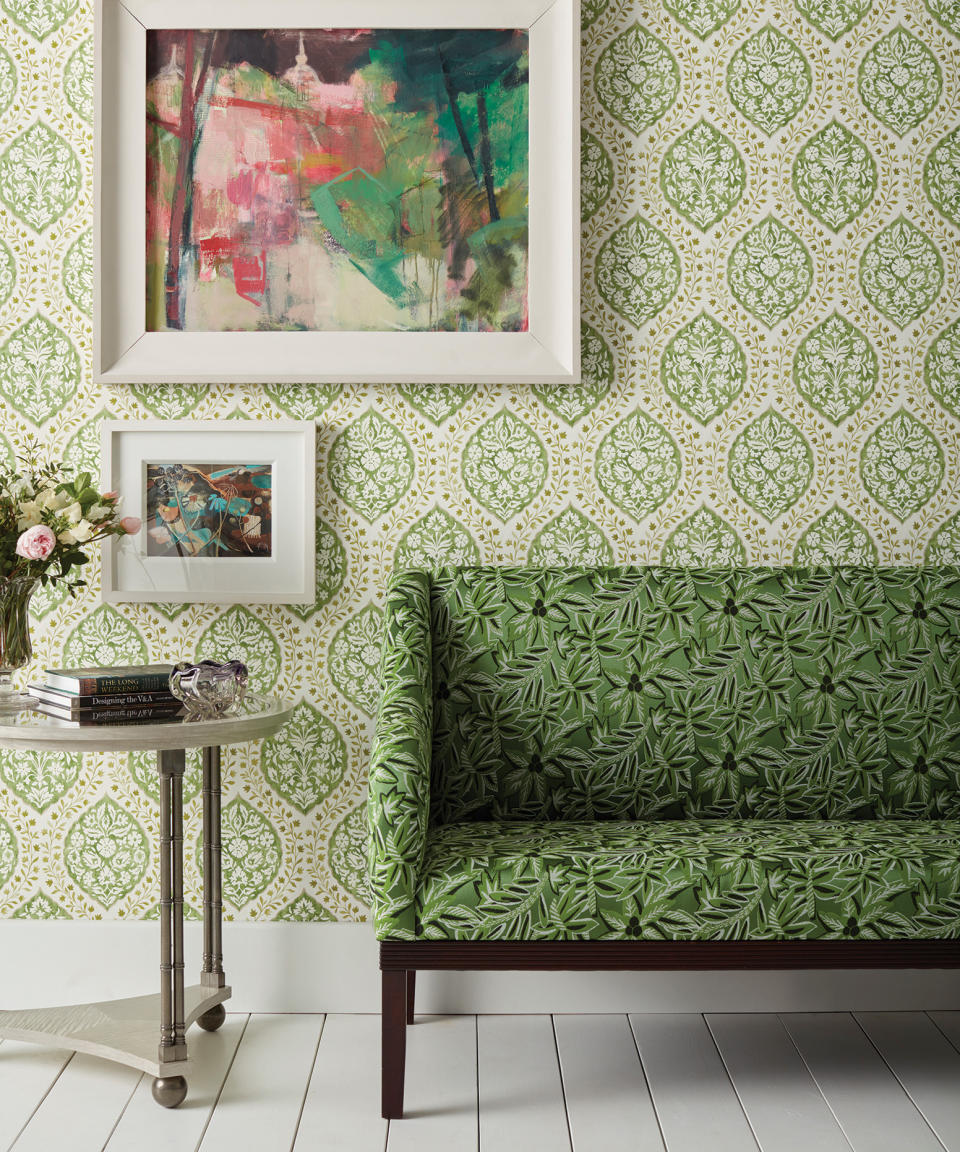 Wallpaper inspiration with a green patterned wallpaper in a living room with white floorboards and a small, green botanical print sofa.