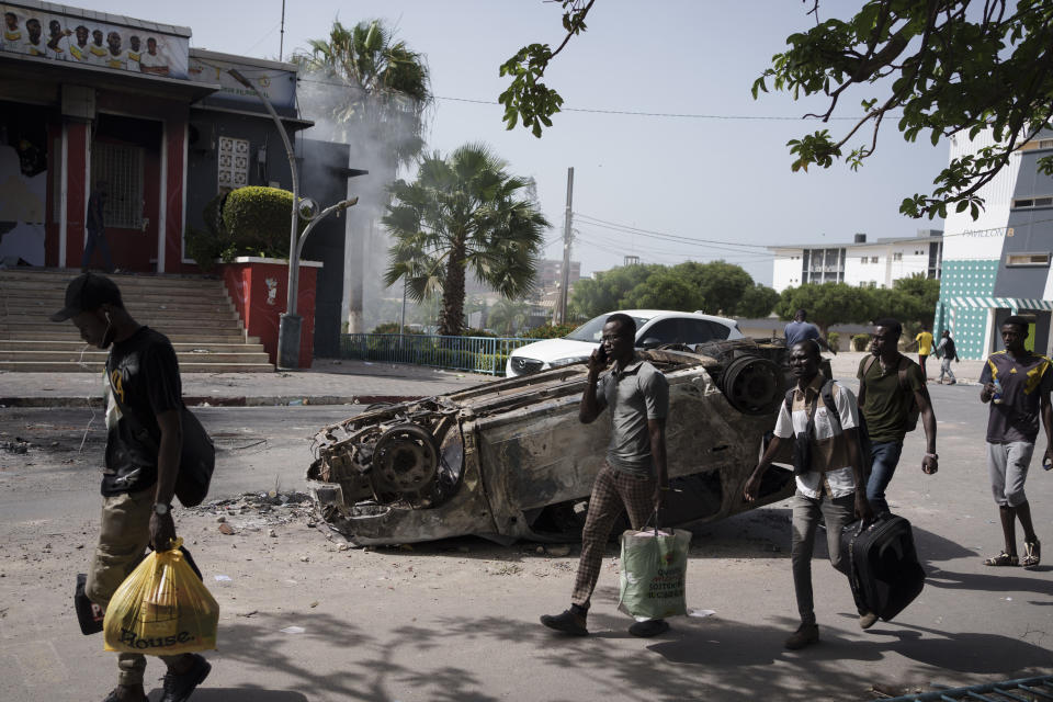 Carrying their belongings students walk past a burned car as they leave the campus of the Cheikh Anta Diop University after authorities ordered the institution to be closed until further notice in Dakar, Senegal, Friday, June 2, 2023. Clashes between police and supporters of Senegalese opposition leader Ousmane Sonko left nine people dead, the government said Friday, with authorities issuing a blanket ban on the use of several social media platforms in the aftermath of the violence. (AP Photo/Leo Correa)