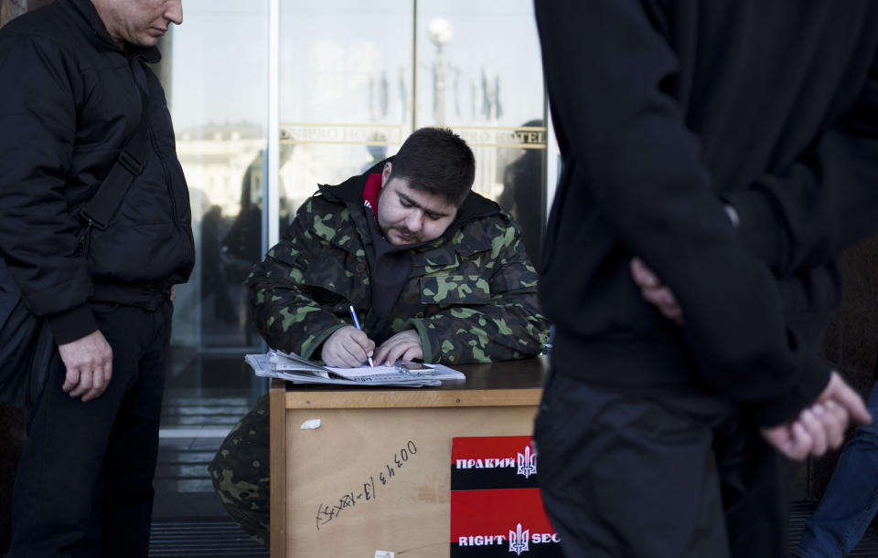 In this photo taken Tuesday, March 11, 2014, a member of the Right Sector registers the details of a man, at left, interested in joining the group outside the Dnipro hotel near Kiev's Independence Square, Ukraine. Having received no posts in the new government, the group is now transforming itself into a political party and plans to field its leader to run in presidential elections in the May 25 election. The Right Sector is also recruiting volunteers to fight Russian troops who have occupied the Black Sea peninsula of Crimea. (AP Photo/David Azia)