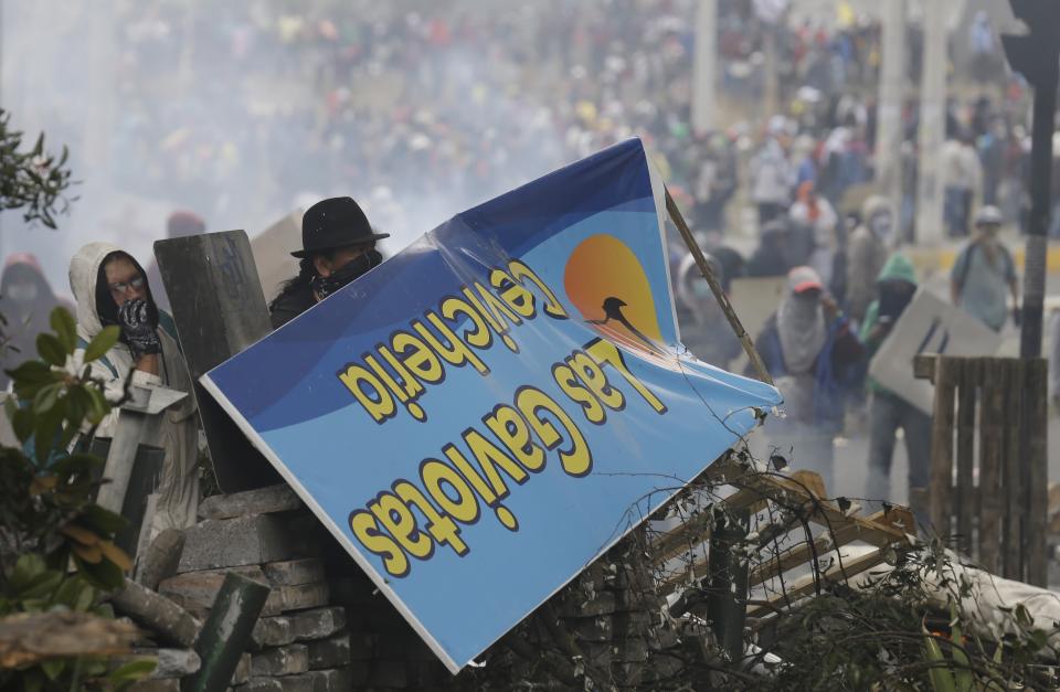 Anti-government demonstrators use a sign for cover at a barricade during clashes with police in Quito, Ecuador, Saturday, Oct. 12, 2019. Protests, which began when President Lenin Moreno's decision to cut subsidies led to a sharp increase in fuel prices, have persisted for days. (AP Photo/Fernando Vergara)