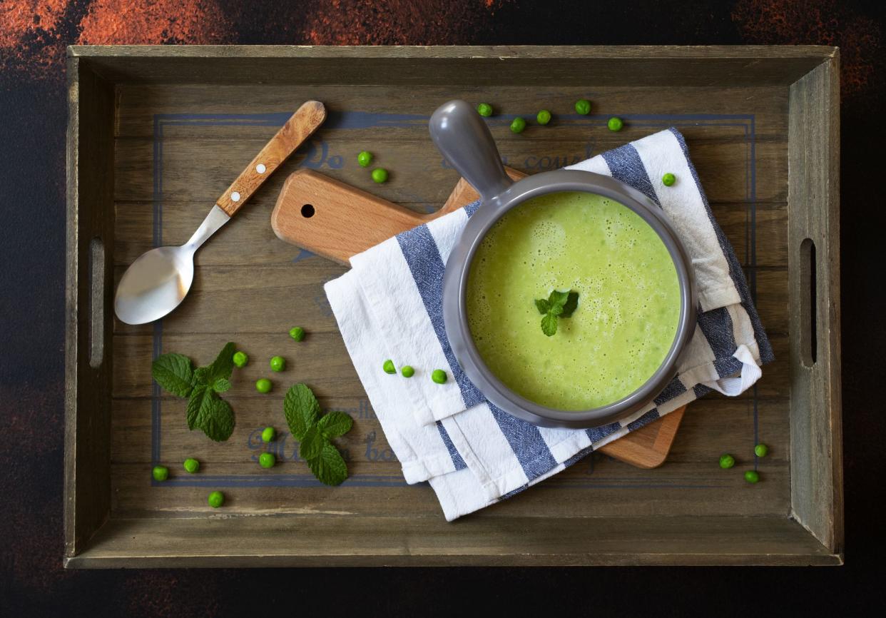 Fresh homemade diet cream soup of green peas and broccoli served with mint on a dark wooden tray. Top view