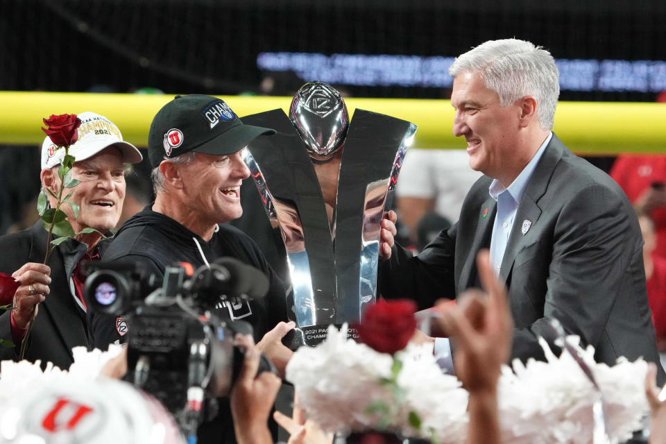 Dec 3, 2021; Las Vegas, NV, USA; Utah Utes head coach Kyle Whittingham is presented the championship trophy by Pac-12 commissioner George Kliavkoff afterthe 2021 Pac-12 Championship Game against the Oregon Ducks at Allegiant Stadium.Utah defeated Oregon 38-10. Mandatory Credit: Kirby Lee-USA TODAY Sports