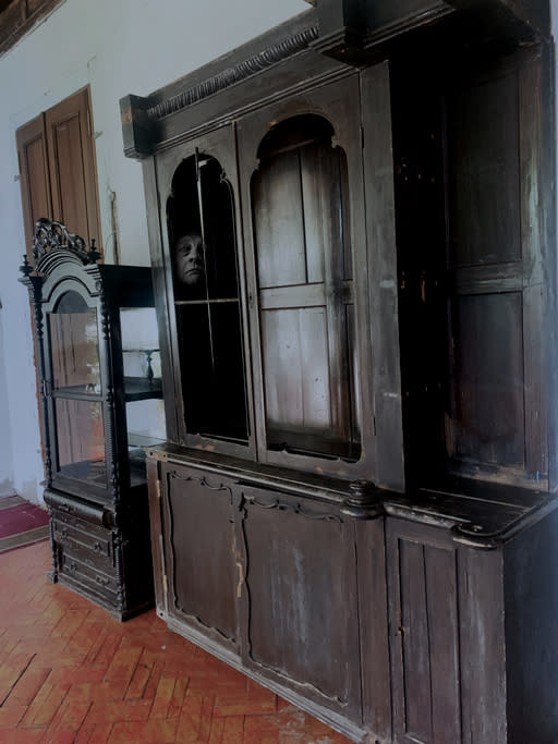 a face showing in the corner of a glass window in an old wooden hutch