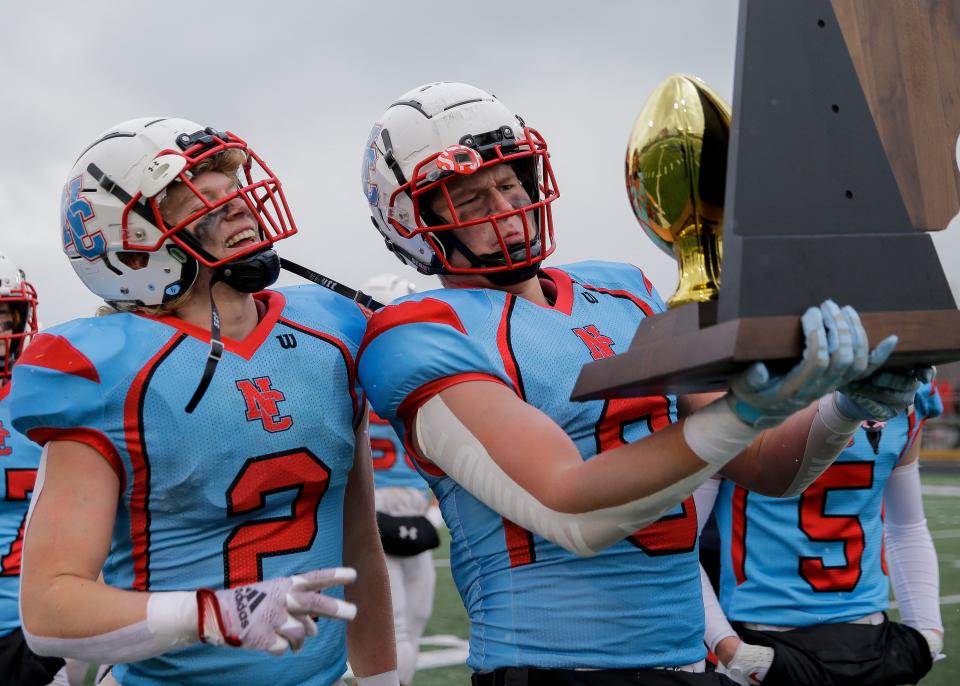 Newman Catholic's Thomas Bates (2) and Eli Gustafson (9) admire their reflections in the championship trophy after beating against Belmont during the WIAA 8-player state championship football game Saturday at South Wood County Stadium in Wisconsin Rapids.