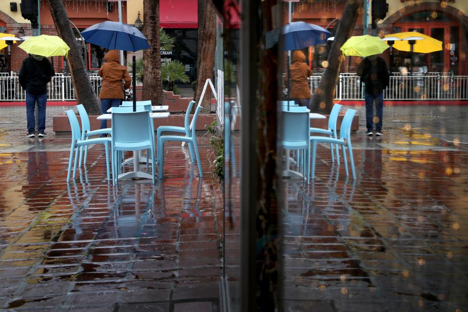 A store front window at La Plaza mirrors the reflection of people holding umbrellas as rain falls in Palm Springs, Calif., on March 1, 2023.