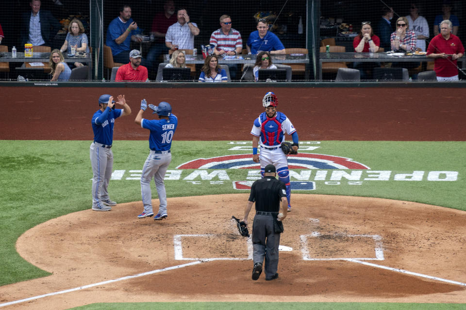 Toronto Blue Jays' Marcus Semien (10) is congratulated by Randal Grichuk after hitting a two-run home run, which scored Grichuk, as Texas Rangers catcher Jose Trevino and home plate umpire Jansen Visconti look on during the second inning of a baseball game Monday, April 5, 2021, in Arlington, Texas. (AP Photo/Jeffrey McWhorter)