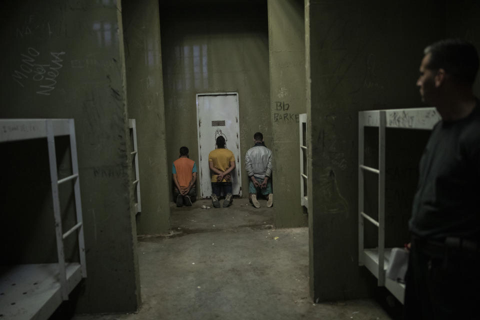 Men kneel with their hands behind their backs at a police station after they were caught robbing a home in Rosario, Argentina, Thursday, Nov. 18, 2021. Rosario is Argentina’s most violent city. (AP Photo/Rodrigo Abd)