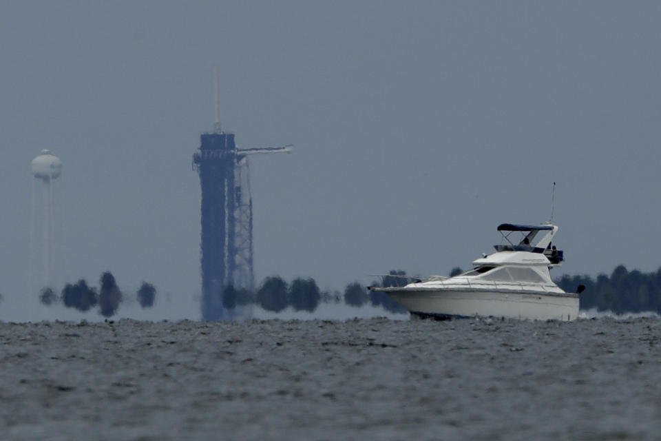 A boat passes the SpaceX Falcon 9 rocket with NASA astronauts Doug Hurley and Bob Behnken in the Dragon crew capsule, as seen from Titusville, Fla. Wednesday, May 27, 2020. The launch of the SpaceX test flight to the International Space Station was scrubbed with more than 16 minutes to go in the countdown due to lightning. (AP Photo/Charlie Riedel)
