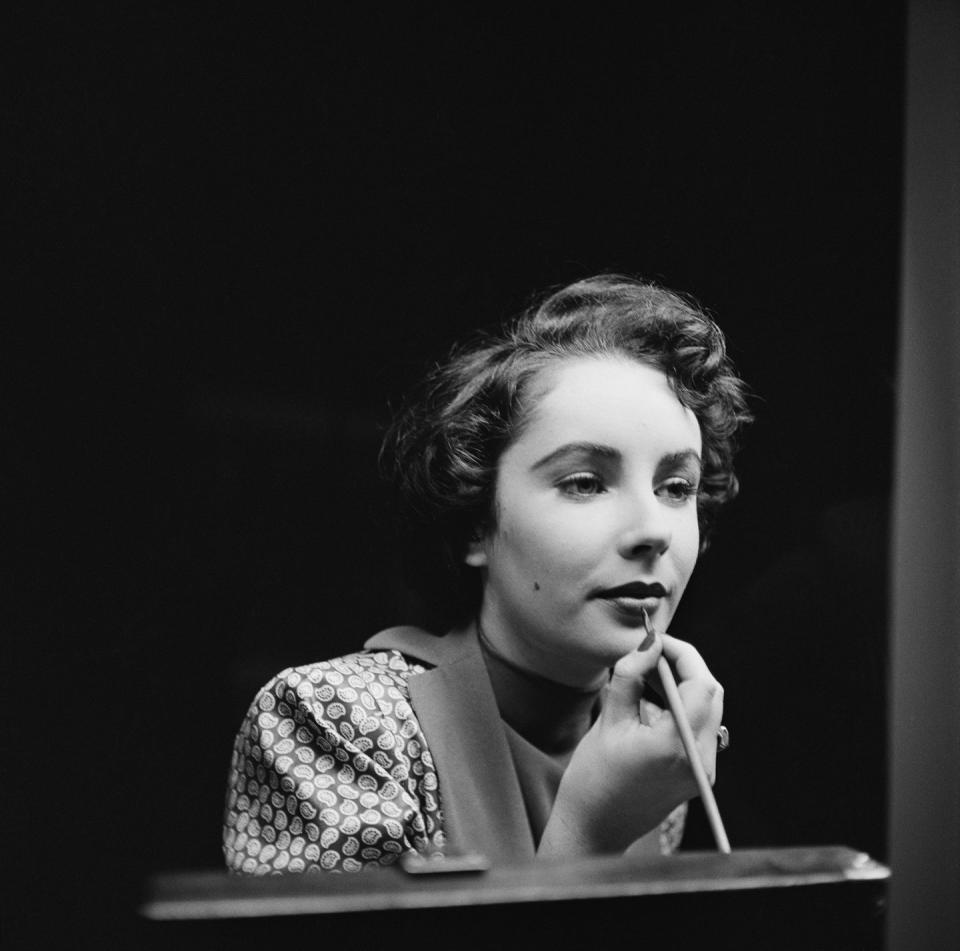 <p>Elizabeth was very skilled at doing her own makeup — and actually preferred doing it herself. Here, the actress is seen putting the final touches on her lips. </p>