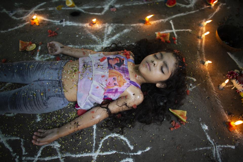 In this photo taken Oct. 13, 2019, girl lies surrounded by candles and designs of white powder during a ceremony on Sorte Mountain where followers of indigenous goddess Maria Lionza gather annually in Venezuela's Yaracuy state. Believers congregated for rituals on the remote mountainside where adherents make an annual pilgrimage to pay homage to the goddess, seeking spiritual connection and physical healing. (AP Photo/Ariana Cubillos)