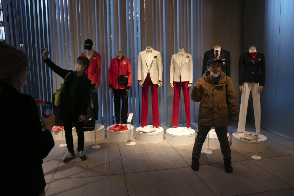 People take pictures in front of the Japanese national team's opening ceremony uniforms for the Tokyo 2020 Olympics and Paralympics Sunday, Feb. 23, 2020, in Tokyo. (AP Photo/Jae C. Hong)