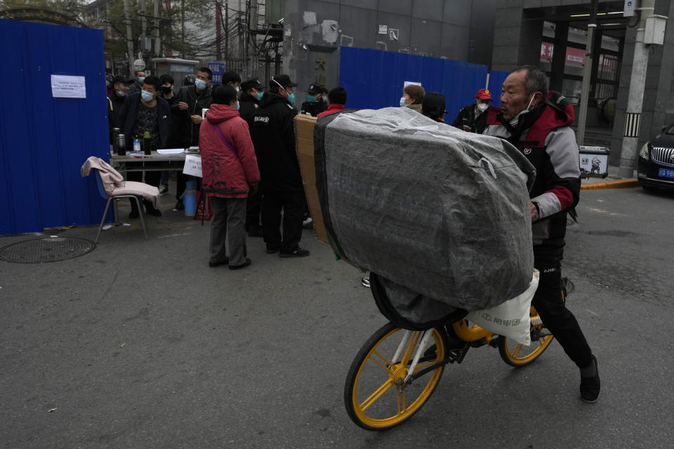 A man carrying a load rides past security guards controling access into a community under lockdown in Beijing, Thursday, Nov. 24, 2022. China is expanding lockdowns, including in a cental city where factory workers clashed this week with police, as its number of COVID-19 cases hit a daily record. (AP Photo/Ng Han Guan)