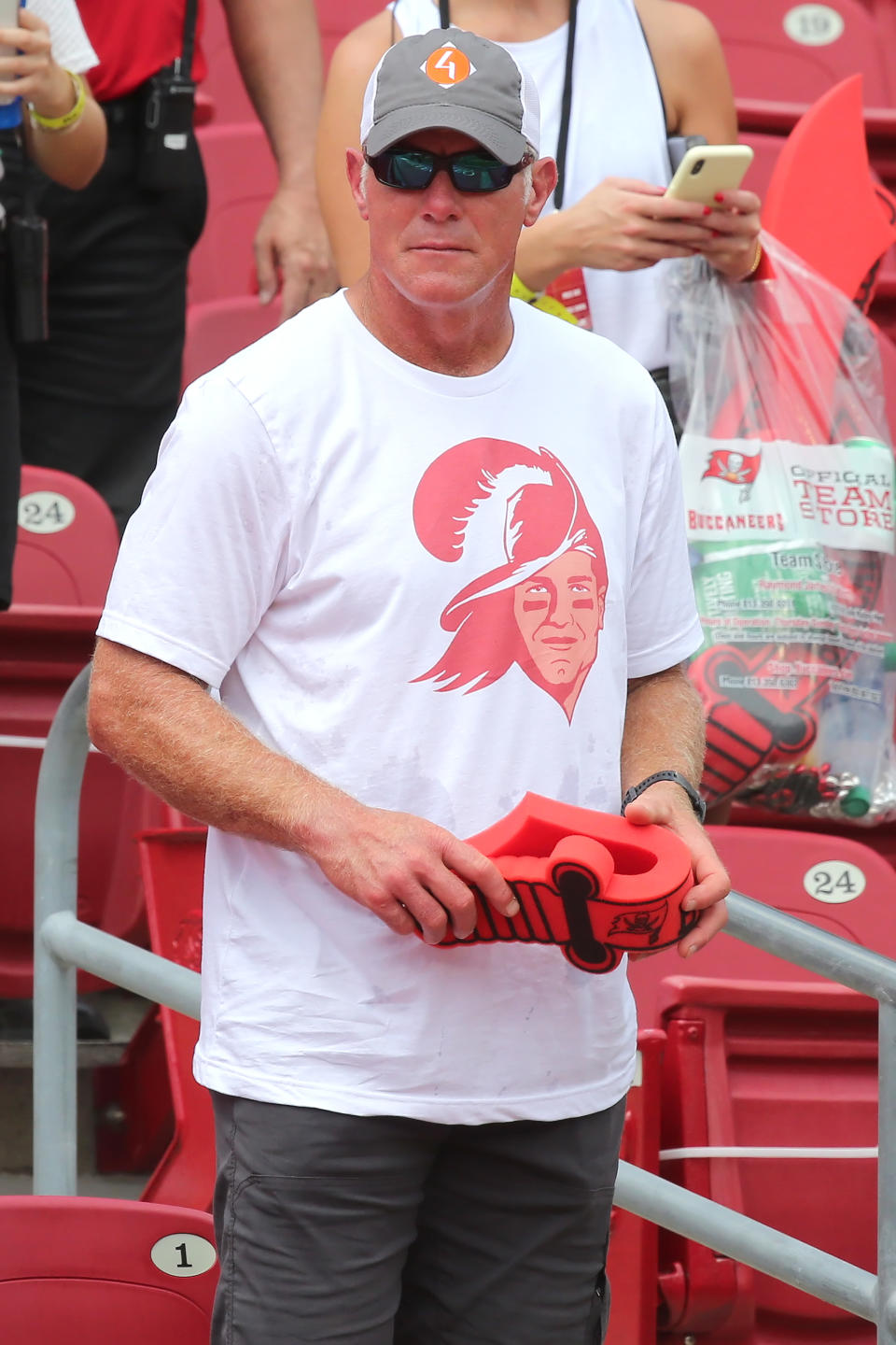 Man in white T-shirt with graphic, holding a red object, standing at a sporting event