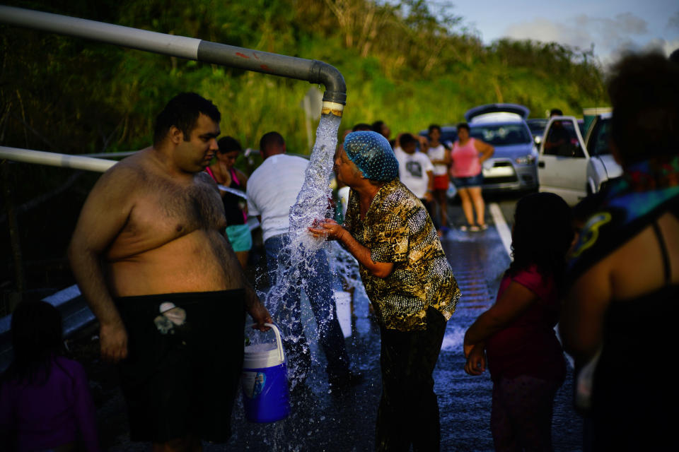 FILE - In this Oct. 14, 2017 file photo, people who lost access to water in the wake of Hurricane Maria gather at pipes carrying water from a mountain creek, on the side of the road in Utuado, Puerto Rico, almost one month after the storm hit. An after-action report by FEMA found it had underestimated the food and fresh water needed, and how hard it would be to get supplies to the island. (AP Photo/Ramon Espinosa, File)