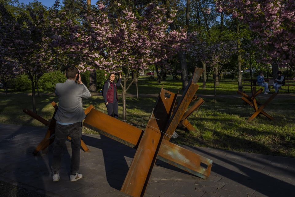 People take pictures next to flowering trees and anti-tank hedgehogs in a park in Kyiv, Saturday, May 6, 2023. (AP Photo/Bernat Armangue)