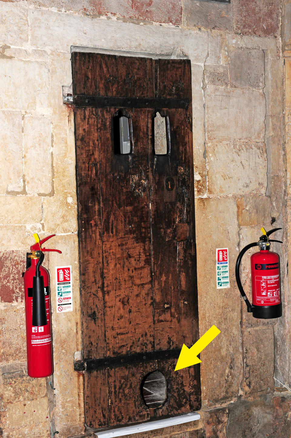 A very old-looking wood door in the middle of a stone wall with a smallish, oblong hole at the bottom