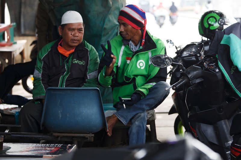 Loro Aji Sayekti, a 34 year-old Gojek motorbike taxi driver gestures as he chats with his friend while waiting for customers on the side road amid the coronavirus disease (COVID-19) outbreak, in Depok