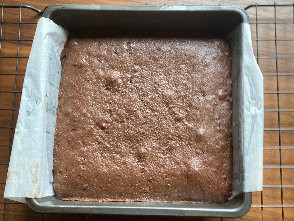 Brownies with a smooth top and some air bubbles in a square pan on a wire rack