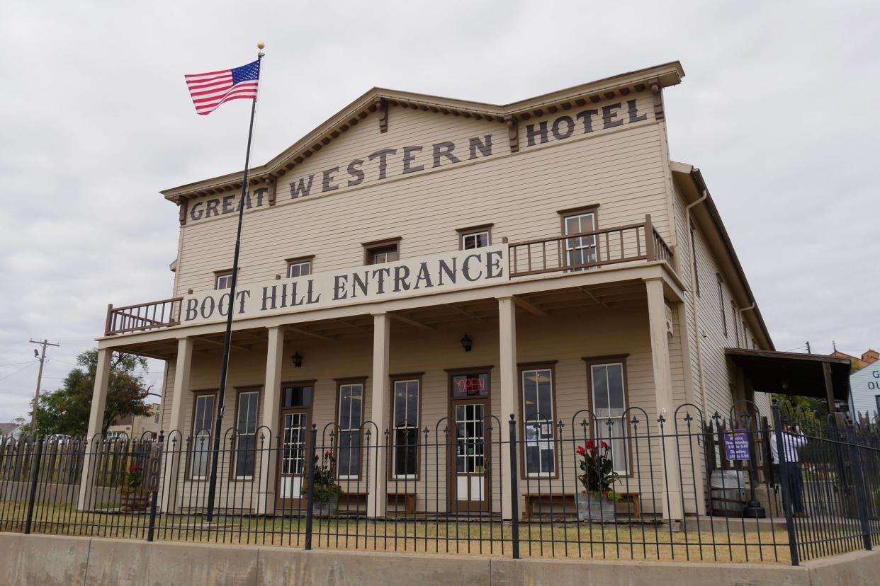 Replica of the Great Western Hotel, Dodge City, Kansas, black fence surrounds it, with an American flag, a grey cloud covered sky in the background