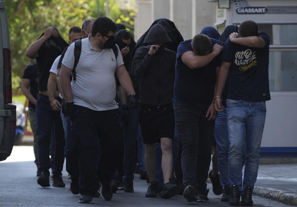 Soccer fans covering their faces, most of them from Croatia, are escorted by police as they leave the Athens Police Headquarters, in Greece, Wednesday, Aug. 9, 2023. Ninety-four fans of Croatia's Dinamo Zagreb are appearing in court this morning for a preliminary hearing over Monday night's fan violence that left a fan of Greece's AEK dead and another eight people injured. (AP Photo/Petros Giannakouris)