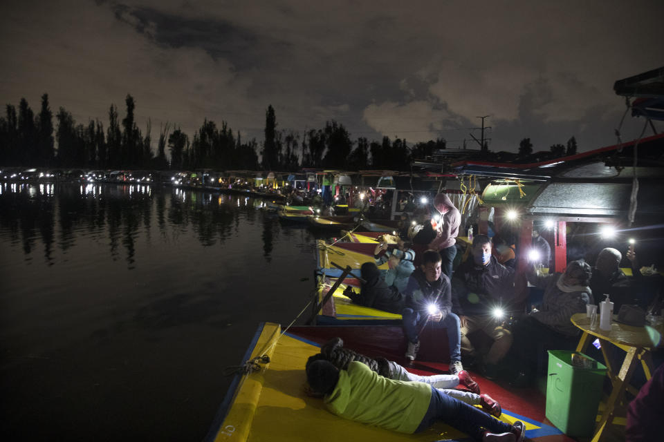 People cast the light of their cellphones from their trajinera boats as they watch the play La Llorona performed on top of a chinampa, a small artificial island at Cuemanco pier in Xochimilco, Mexico City, late Friday, Oct. 9, 2020, as the city promotes the upcoming Day of the Dead holiday at the end of the month, amid the COVID-19 pandemic. Legend has it that La Llorona drowned her children and then regretfully looks for them in rivers and towns, scaring locals who can hear her at night. (AP Photo/Marco Ugarte)