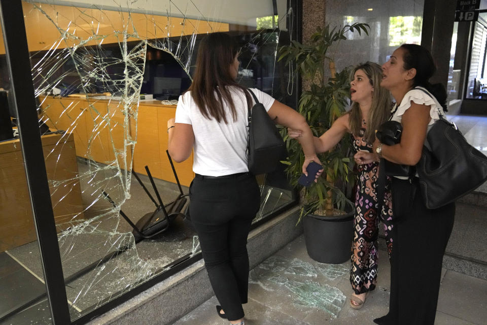 Panicked bank employees stand next to a window that was broken by attackers to exit the bank, in Beirut, Lebanon, Wednesday, Sept. 14, 2022. An armed woman and a dozen activists broke into a Beirut bank branch on Wednesday, taking over $13,000 from what she says were from her trapped savings. Lebanon's cash-strapped banks since 2019 have imposed strict limits on withdrawals of foreign currency, tying up the savings of millions of people. (AP Photo/Hussein Malla)