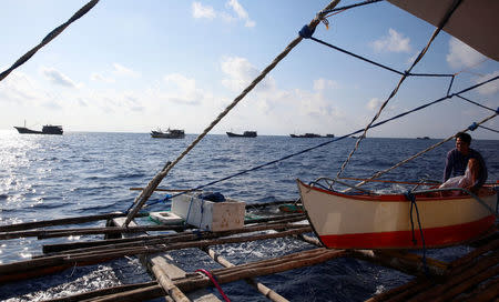 A Philippine fisherman rests on a dinghy as Chinese fishing boats pass by at the disputed Scarborough Shoal April 5, 2017. Picture taken April 5, 2017. REUTERS/Erik De Castro