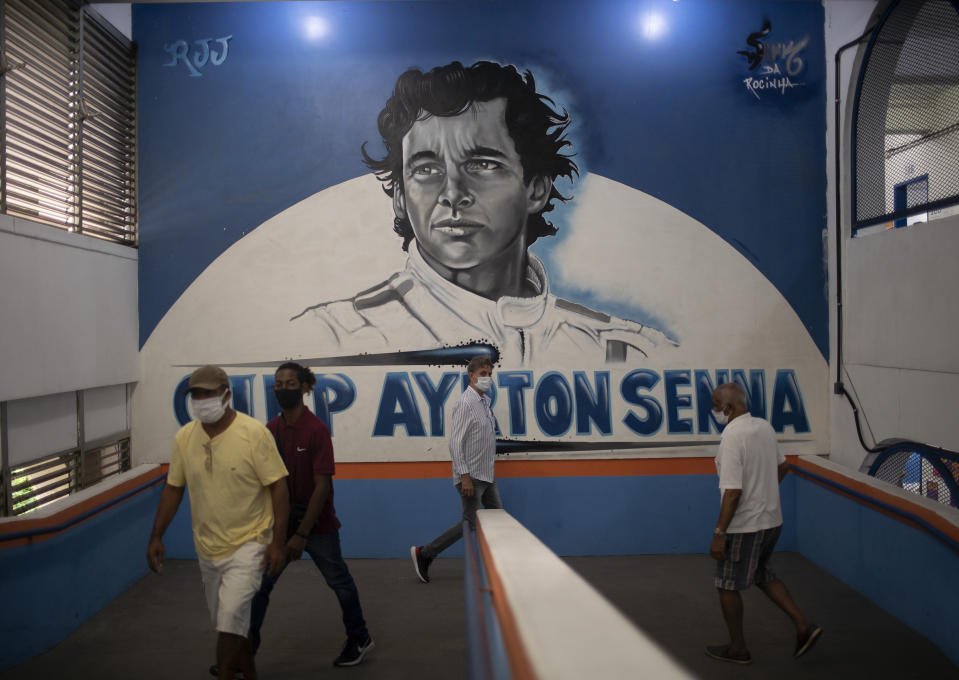 Residents enter a school where a mural of Brazil's late Formula One driver Ayrton Senna covers the wall during municipal elections, at a polling station in the Rocinha slum of Rio de Janeiro, Brazil, Sunday, Nov.15, 2020. Voters across Latin America's biggest country are electing mayors and municipal council members. (AP Photo/Silvia Izquierdo)