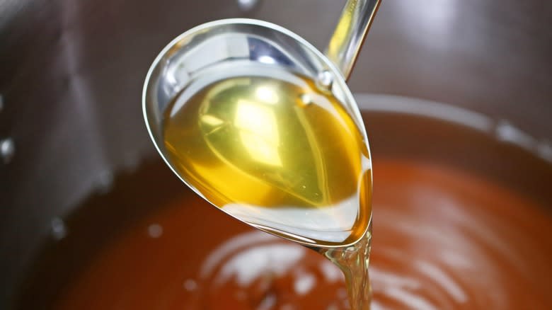 Close-up of a ladle pouring beef broth into a pot