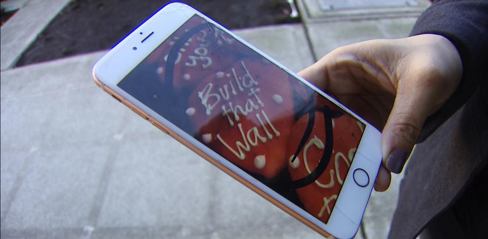In this Jan. 24, 2019, video image provided by KING-TV, Ana Carrera shows her phone with a photo of cookies she posted in Facebook, after she took the picture at Edmonds Bakery in Edmonds, Wash. Ken Bellingham, who owns the bakery, is apologizing for a politically charged Valentine's Day cookie that generated an uproar on social media. KING-TV reports that Bellingham has gotten phone calls from frustrated customers about the heart-shaped cookie with "Build that Wall" in frosting letters. The wall refers to President Donald Trump's signature campaign promise to build a southern-border wall. (KING-TV via AP)