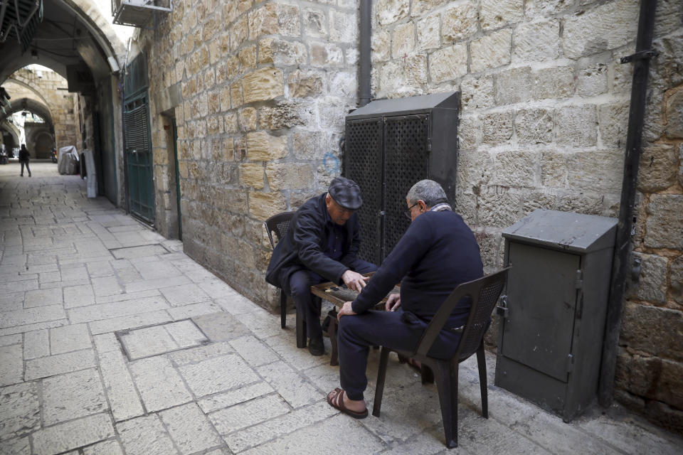 In this Thursday, March 26, 2020 photo, Palestinians play a board game in a deserted Old City in Jerusalem. As the coronavirus spreads across the Middle East, cherished traditions are coming to an abrupt halt: No more coffee shops where men gather to play cards and backgammon. (AP Photo/Mahmoud Illean)