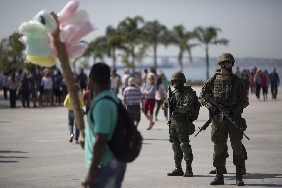 Soldiers stand guard in Maua square where a cotton candy vendor passes by in Rio de Janeiro