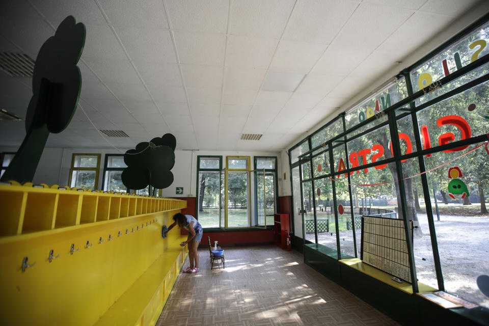 A worker cleans the coat rack in the 'La Giostra Nel Parco' (Merry go around in the park) nursery school in Milan, northern Italy, Thursday, Aug. 27, 2020, ahead of reopening. Despite a spike in coronavirus infections, authorities in Europe are determined to send children back to school. Italy, Europe’s first virus hot spot, is hiring 40,000 more temporary teachers and ordering extra desks, but some won’t be ready until October. (AP Photo/Luca Bruno)