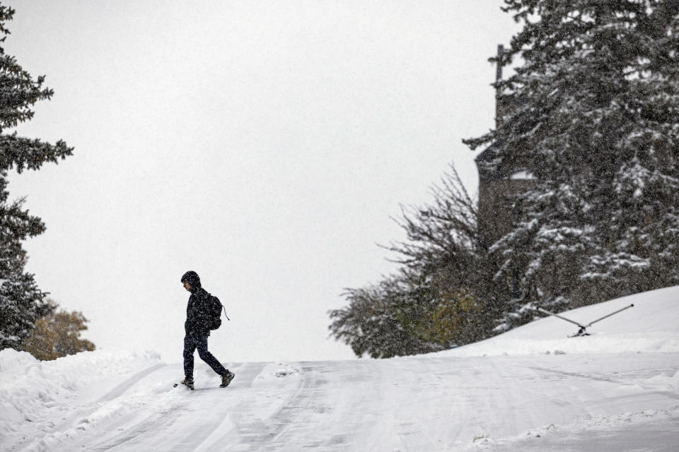 A pedestrian crosses a snow-covered road, Wednesday, Oct. 25, 2023, in Helena, Mont. The first major snowstorm of the season dropped up to a foot of snow in the Helena area by Wednesday morning, canceling some school bus routes. (Thom Bridge/Independent Record via AP)