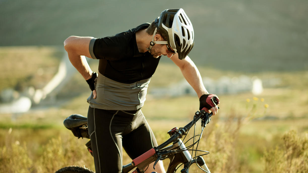 Shot of a mature man experiencing back pain while out for a ride on his mountain bike.