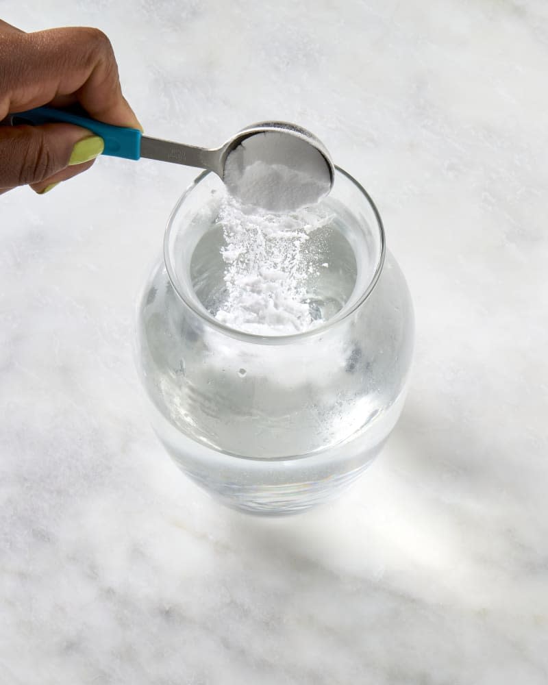 angled shot of baking soda being poured into warm water in a vase