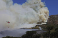 A helicopter drops water over a fire at Rhodes Memorial on Table Mountain, Cape Town, South Africa, Sunday, April 18, 2021. A wildfire raging on the slopes of the mountain forced the evacuation of students from the University of Cape Town. (AP Photo/Nardus Engelbrecht)