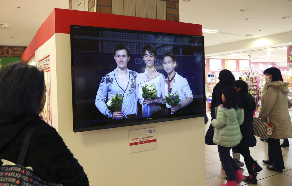 A woman watches a public TV showing recordings of men's figure Skating Singles medalists, gold medalist Yuzuru Hanyu of Japan, center, silver medalist Patrick Chan of Canada, left, and bronze medalist Denis Ten of Kazakhstanat, at a special Sochi olympic booth at Tokyo Station in Tokyo, Saturday, Feb. 15, 2014. Japan celebrated Hanyu's historic win in men's figure skating at the break of dawn Saturday, rejoicing in the country's first-ever gold medal in the Olympic event. (AP Photo/Koji Sasahara)