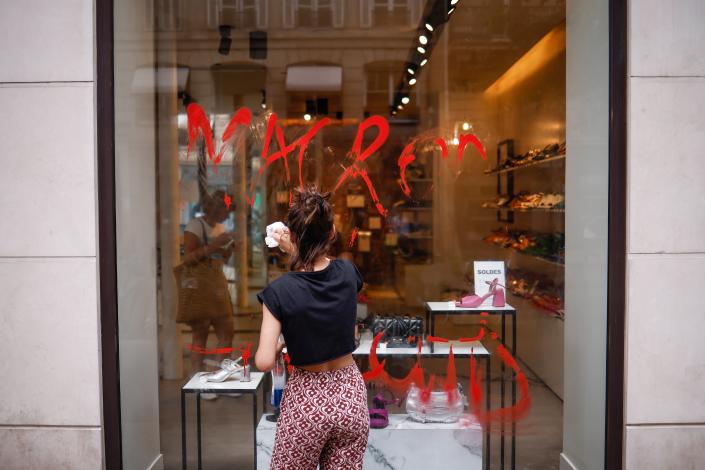 A shopkeeper cleans a Macron graffiti written on the storefront in Paris, France, 30 June 2023 (EPA)