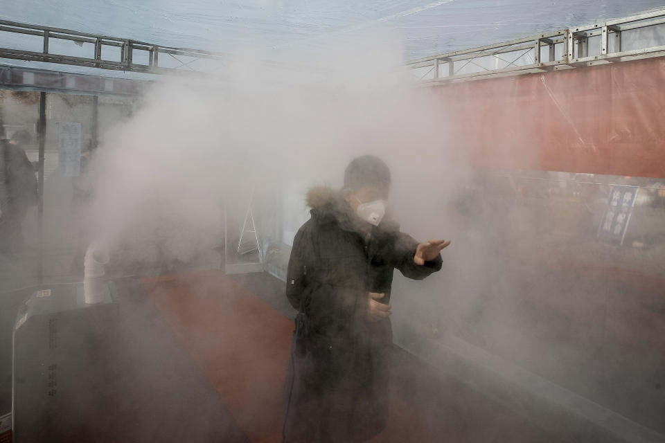 A man walks through a disinfectant spray in order to return home at a residential complex in northern China's Tianjin Municipality Tuesday, Feb. 11, 2020. China's daily death toll from a new virus topped 100 for the first time and pushed the total past 1,000 dead, authorities said Tuesday after leader Xi Jinping visited a health center to rally public morale amid little sign the contagion is abating. (Chinatopix Via AP) CHINA OUT