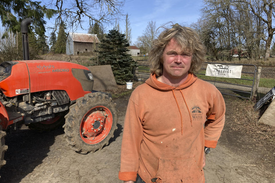 Aaron Nichols poses next to his tractor on March 17, 2023, in the unincorporated community of Helvetia, Ore. Nichols believes that a bill in the Legislature that would allow the governor to unilaterally expand urban growth boundaries threatens farms. (AP Photo/Andrew Selsky)