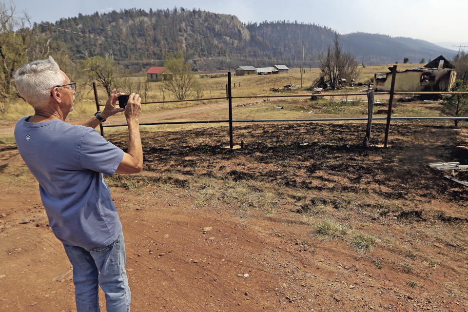 A.B. Montoya takes a photo of a building that was completely burned in the Calf Canyon Fire in Rociada, N.M., Tuesday, May 10, 2022. The former owner of this house was related to his dad. The largest wildfire burning in the United States was heading toward mountain resort towns in northern New Mexico on Wednesday, prompting officials to issue another set of warnings for more people to prepare to evacuate as the fast-moving fire picks up momentum. (Luis Sanchez Saturno/The New Mexican via AP)