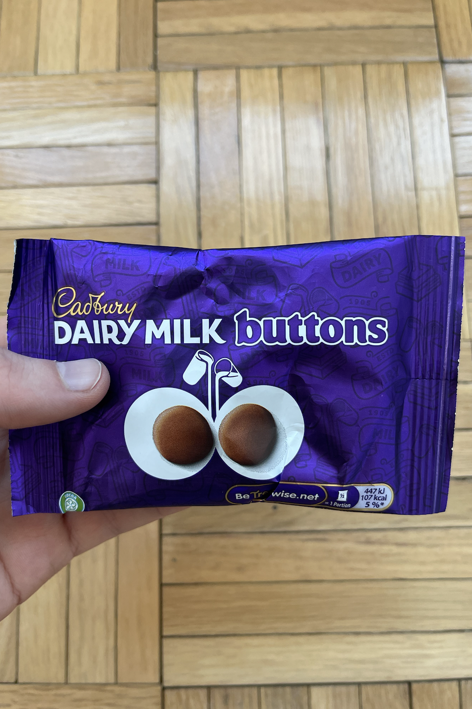 Hand holding a Cadbury Dairy Milk Buttons pack with two chocolate pieces shown on the front