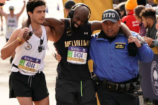 <p>TIMOTHY A. CLARY/AFP via Getty</p> A runner is helped across the finish line during the 2021 TCS New York City Marathon