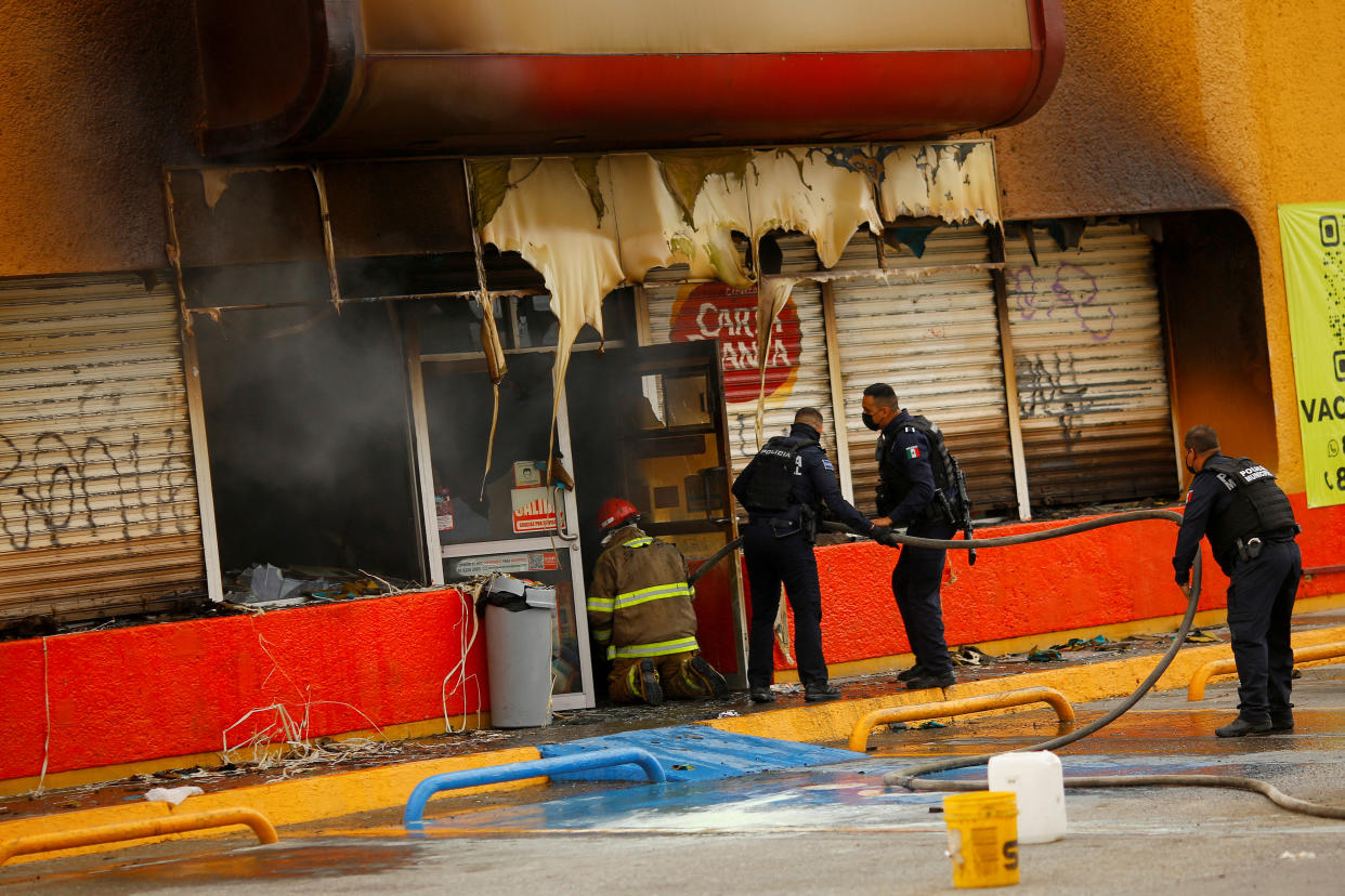 Firefighters and police officers insert a hose inside a convenience store that was burned by unknown attackers, in a simultaneous attack of fires in different parts of the city, according to local media, in Ciudad Juarez, Mexico, August 11, 2022. REUTERS/Jose Luis Gonzalez